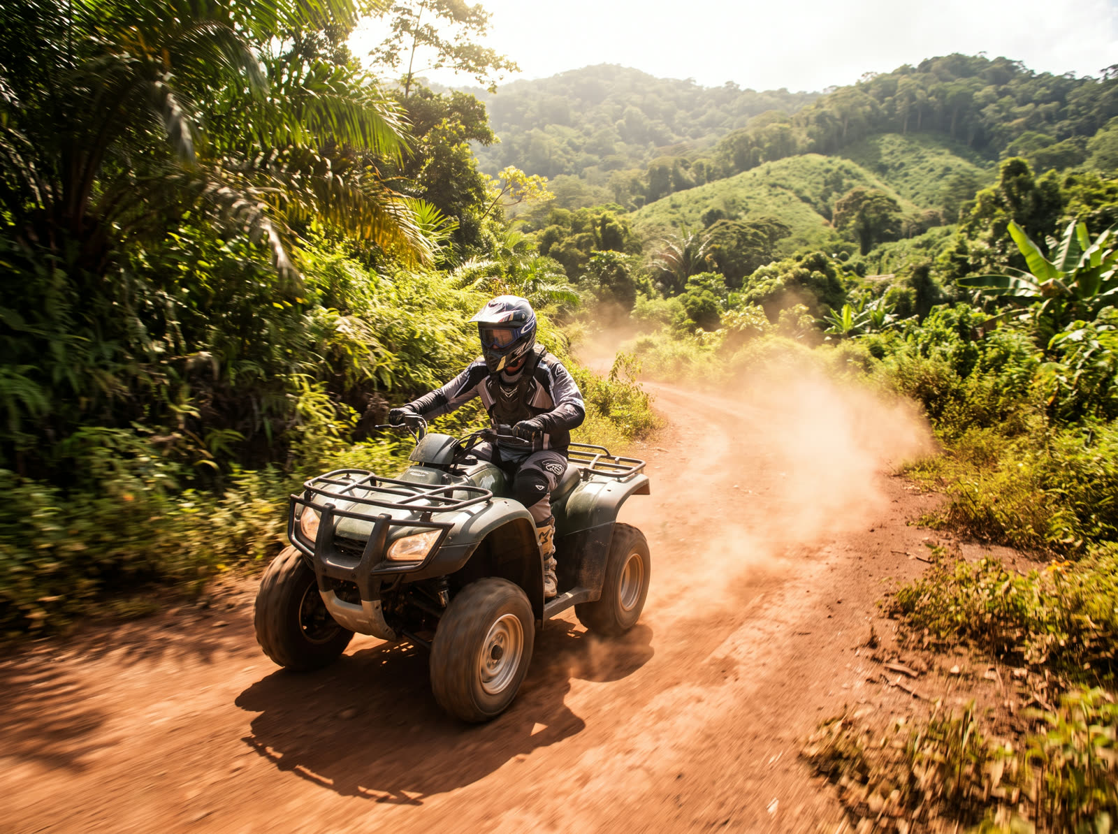 A rider on a quad bike kicking up dust on a sunlit jungle trail